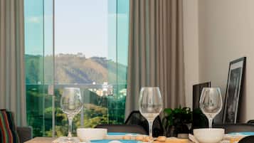 Una mesa de comedor con platos, tazones y copas de vino, con vistas panorámicas de colinas a través de amplios ventanales.