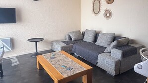 Un salon moderne avec un canapé d’angle, une table basse en bois, une petite table ronde et des œuvres d’art décoratives accrochées au mur.