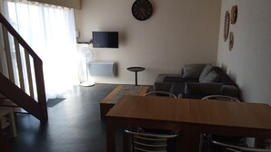 Un salon avec une table en bois, un canapé, un téléviseur et une horloge au mur.