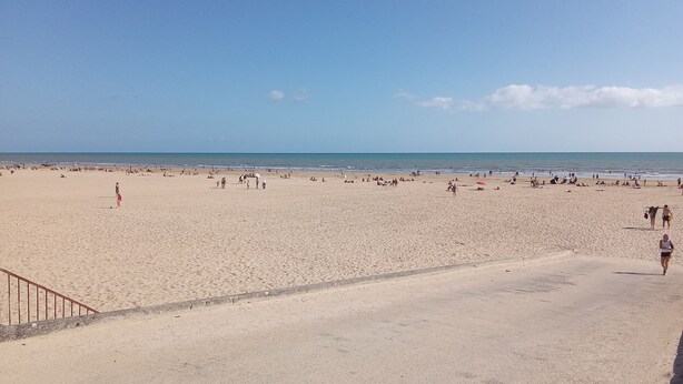 Une vaste plage de sable fin, avec un ciel dégagé et une mer calme.