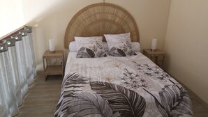 Une chambre à coucher avec un grand lit, deux tables de chevet et une tête de lit en osier.