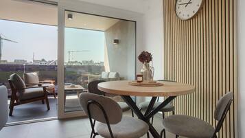 A modern dining area with a round table, four chairs, a clock, and a view of construction cranes outside.