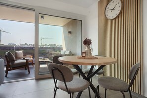 A modern dining area with a round table, four chairs, a clock, and a view of construction cranes outside. - Apartment 'Herzensprojekt' with Balcony and Wi-Fi (Pfullendorf)