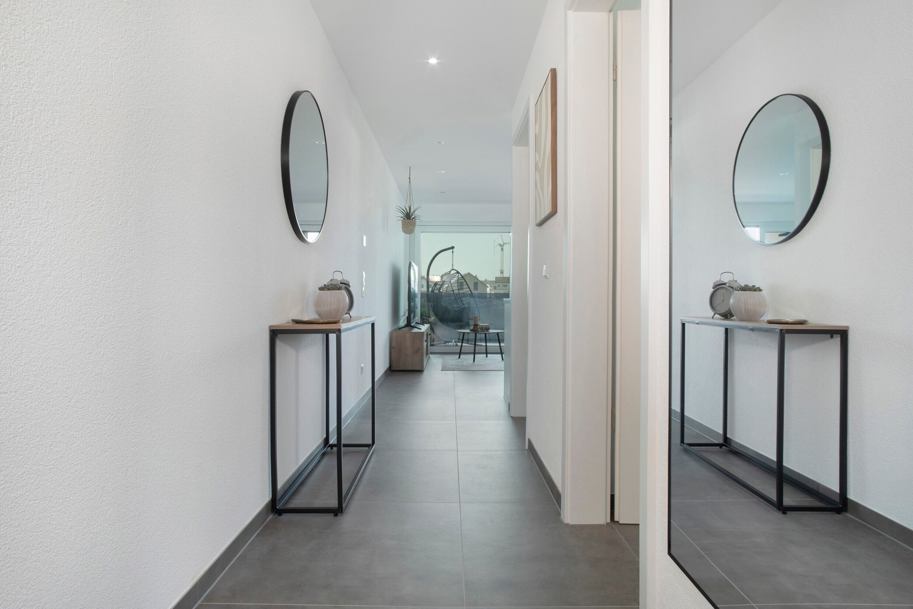 A hallway with a mirrored wall, a small table with a bowl, and a potted plant.