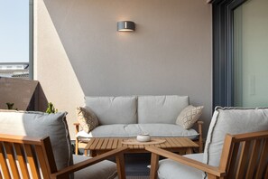 Un balcon avec un canapé, des chaises en bois, une petite table et un luminaire fixé au mur.