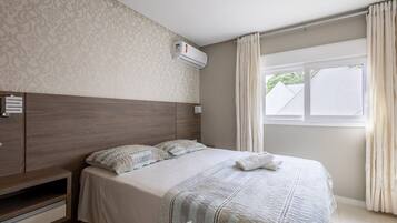 Quarto com cabeceira de madeira, cama com manta listrada, mesa de cabeceira e janela com cortinas.