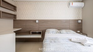 A modern bedroom with a wooden headboard, a built-in bedside table, a bed with a quilted duvet, and an air conditioning unit on the wall. - Sea View Apartment w Barbecue in Bombinhas Lga0201 (Bombinhas)