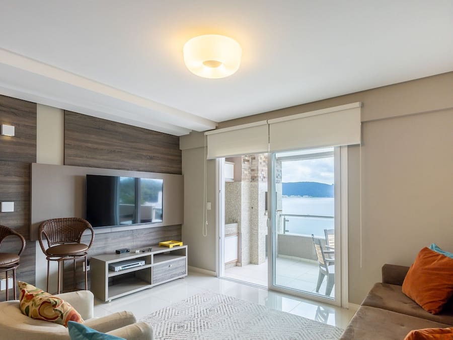 Una sala de estar moderna con televisor de pantalla plana, sillones de mimbre, sofá y un balcón con vistas al mar.
