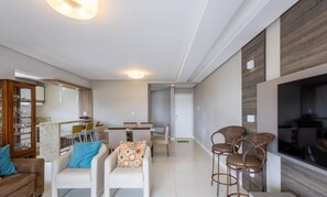 A modern living room with a sofa, armchairs, a dining area, and a TV. - Sea View Apartment w Barbecue in Bombinhas Lga0201 (Bombinhas)