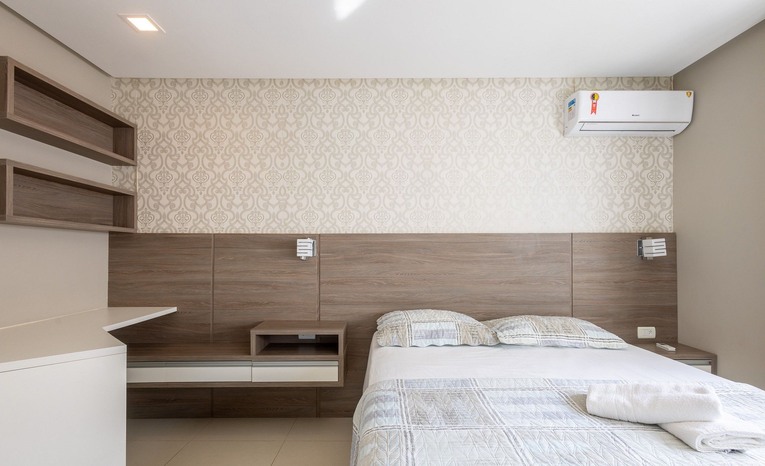 Un dormitorio moderno con cabecera de madera, mesita de noche integrada, cama con edredón acolchado y unidad de aire acondicionado en la pared.