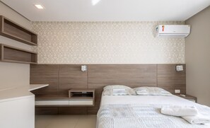 A modern bedroom with a wooden headboard, a built-in bedside table, a bed with a quilted duvet, and an air conditioning unit on the wall. - Sea View Apartment w Barbecue in Bombinhas Lga0201 (Bombinhas)