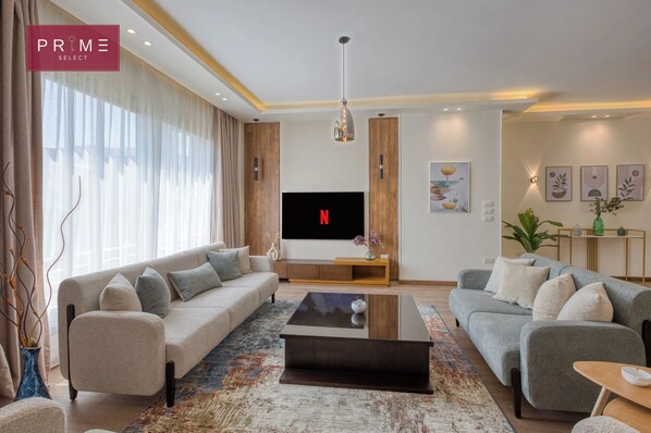 A modern living room with a large flat-screen TV, two sofas, a coffee table, and a decorative plant. - Prime Select Village Gardens Kattameya (New Cairo)