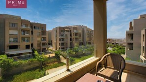 A balcony with wicker furniture, a clear view of neighboring apartment buildings, and a sign reading "PRIME SELECT".