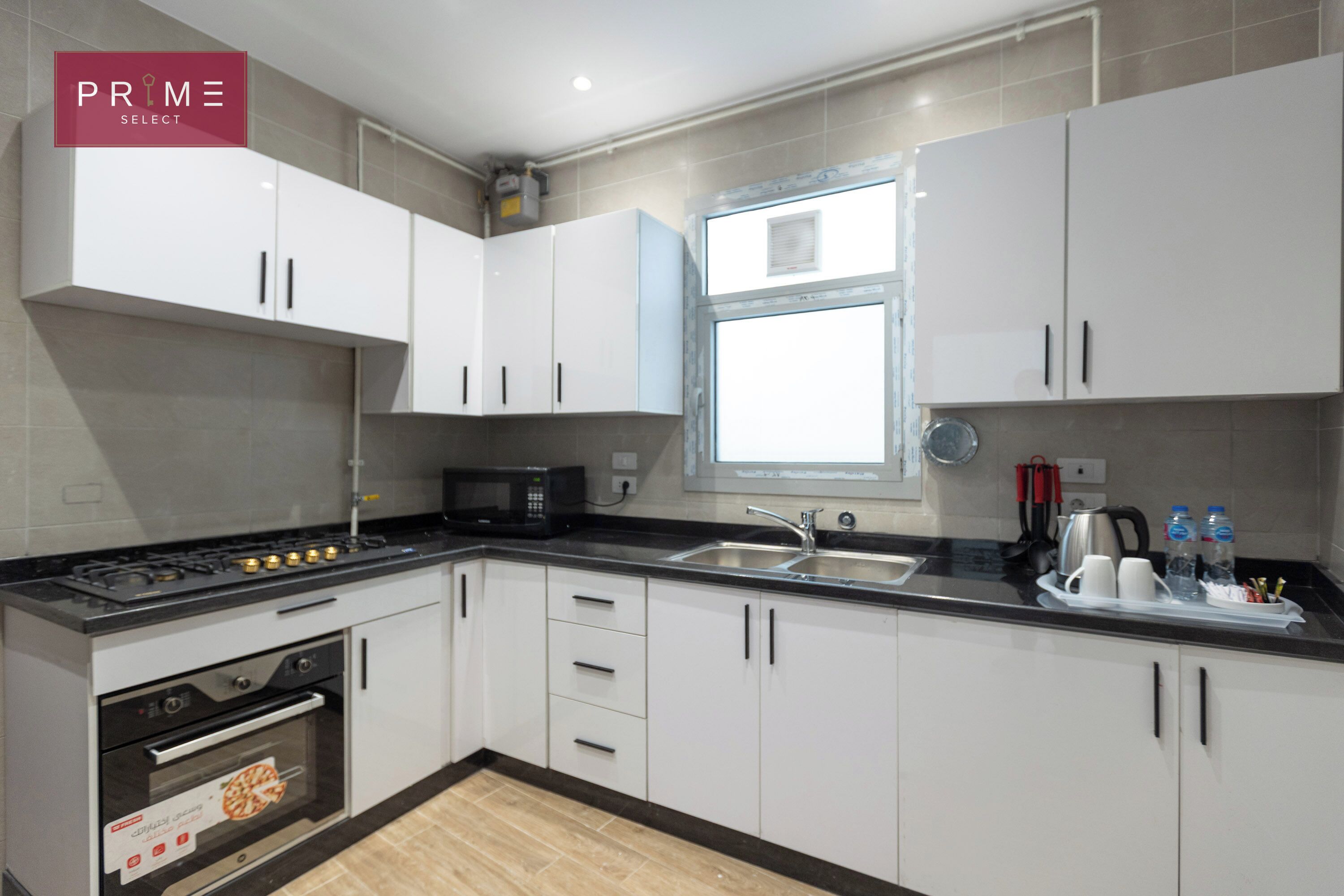 A modern kitchen with white cabinets, a black countertop, a stove, and a window.