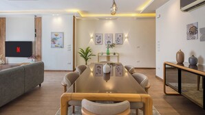 Ein modernes Wohnzimmer mit Holzesstisch, grauem Sofa und einem Flachbildfernseher.