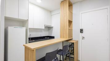 A compact kitchen with white cabinets, a wooden countertop, and a built-in stove. There are two black chairs and a small wooden shelf.