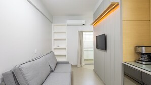 A modern living room with a grey sofa, a flat-screen TV mounted on the wall, and a coffee machine on a counter. - Fully Equipped Accommodations in the Heart of Brasilia LEC (Sudoeste e Octogonal)