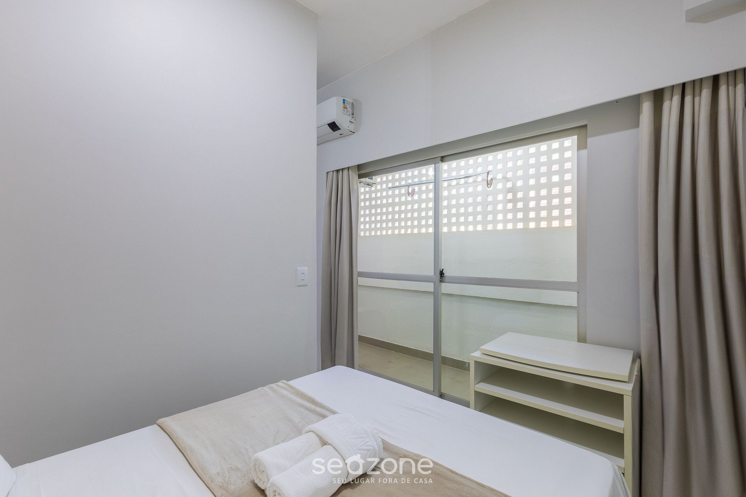 A hotel room with a bed, a small table, a window with a view, and an air conditioning unit.