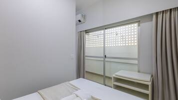 A hotel room with a bed, a small table, a window with a view, and an air conditioning unit.