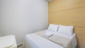 A neatly made bed with white linens and a beige throw blanket, a wooden headboard, and a white bedside table. - Fully Equipped Accommodations in the Heart of Brasilia LEC (Sudoeste e Octogonal)