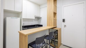 A compact kitchen with white cabinets, a wooden countertop, and a built-in stove. There are two black chairs and a small wooden shelf. - Fully Equipped Accommodations in the Heart of Brasilia LEC (Sudoeste e Octogonal)