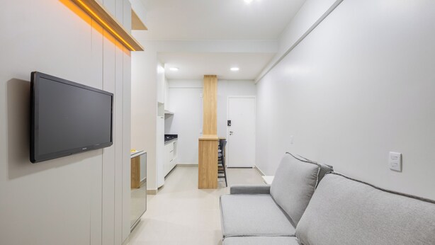 A modern living room with a flat-screen TV mounted on the wall, a grey sofa, and a wooden accent wall. - Fully Equipped Accommodations in the Heart of Brasilia LEC (Sudoeste e Octogonal)