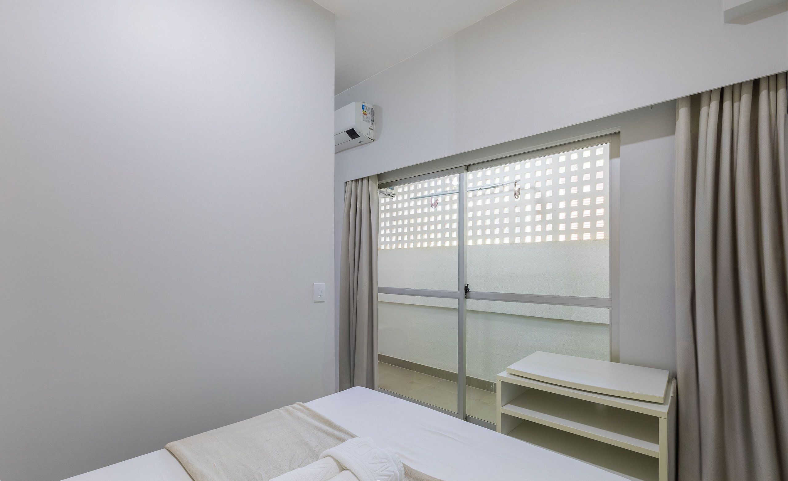 Una habitación de hotel con cama, una mesita, una ventana con vistas y un equipo de aire acondicionado.