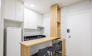Een kleine keuken met witte kastjes, een houten aanrechtblad en een inbouwfornuis. Er staan twee zwarte stoelen en een klein houten plankje.