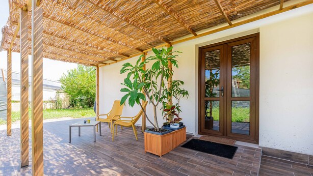 A covered patio area with wooden flooring, a table, chairs, and potted plants.