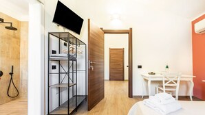 A hotel room with a shower, a TV mounted on the wall, a desk with a chair, and a bed with towels.