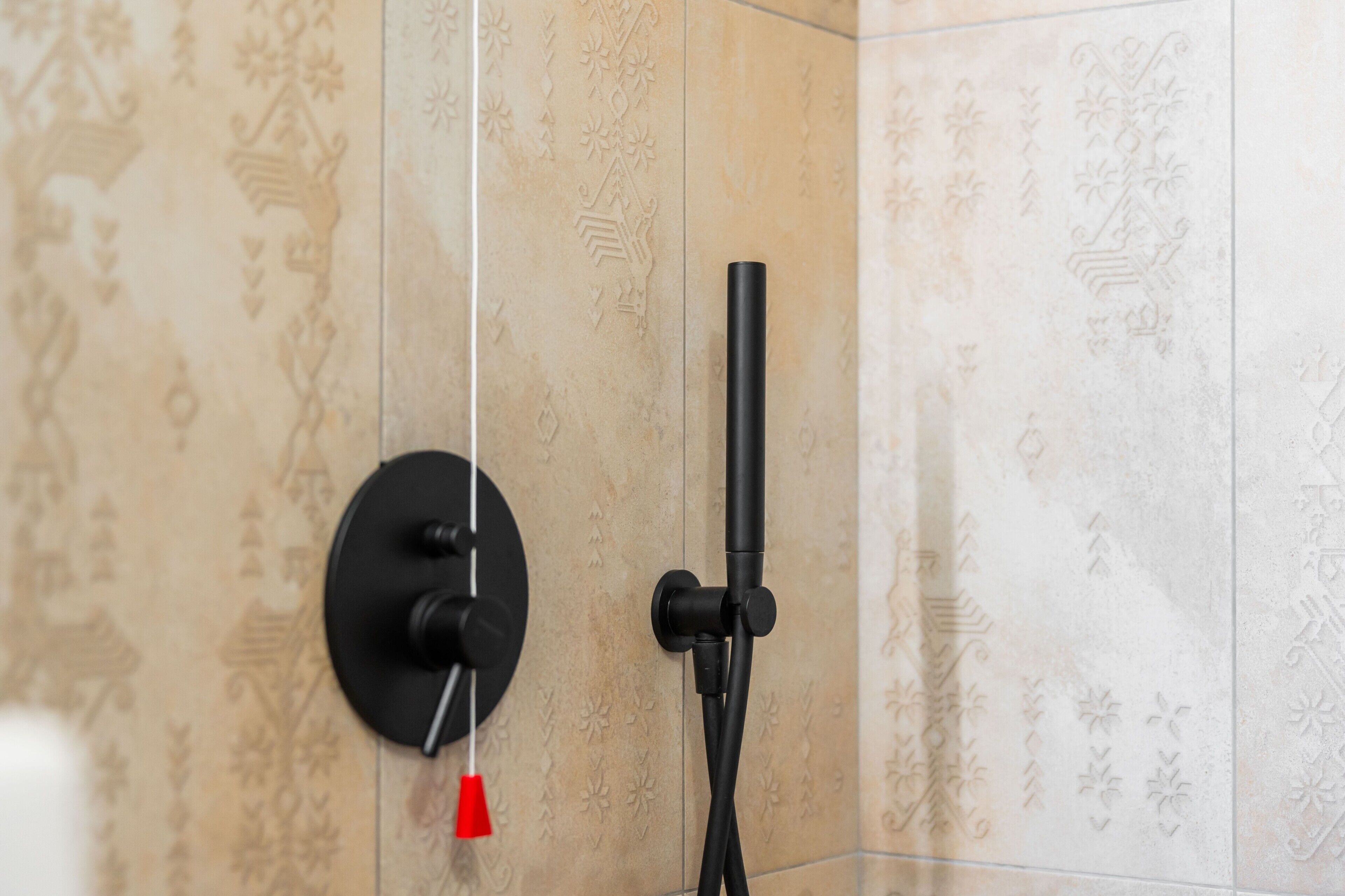 A bathroom with a shower head mounted on a wall with decorative tiles.