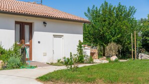 A white building with a tiled roof, a wooden door, and a small garden with plants and a hose.