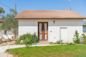 Un petit bâtiment d’un seul étage, doté d’un toit recouvert de tuiles, d’une porte en bois et d’un petit jardin agrémenté de diverses plantes.