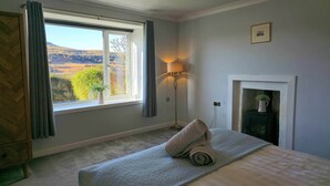 A bedroom with a large window, a floor lamp, a fireplace, and a bed with a rolled towel. - The perfect base for exploring the island with your family. (Portree)