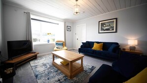 A living room with a television, wooden coffee table, blue sofa, and a large window. - The perfect base for exploring the island with your family. (Portree)