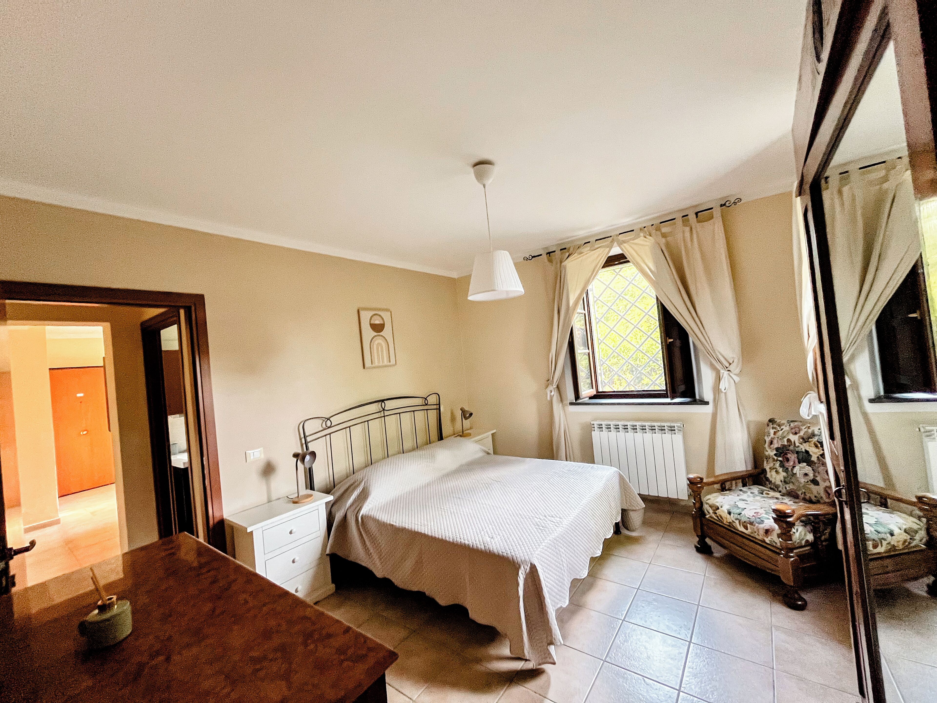 Une chambre à coucher avec un lit, une table de chevet, une chaise et une fenêtre avec des rideaux.