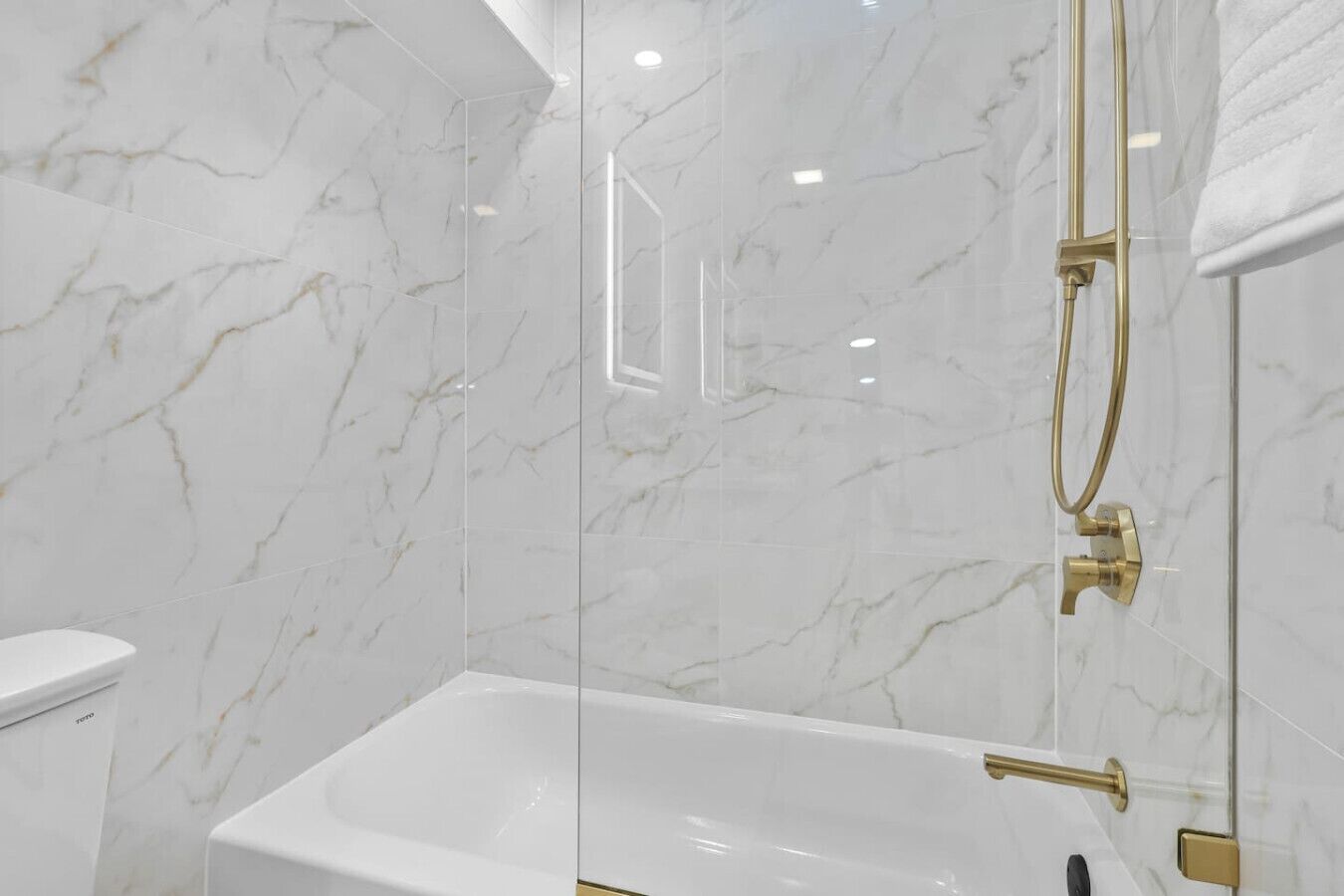 Ein modernes Badezimmer mit einer gläsernen Duschkabine, einer weißen Badewanne und Marmorwänden.