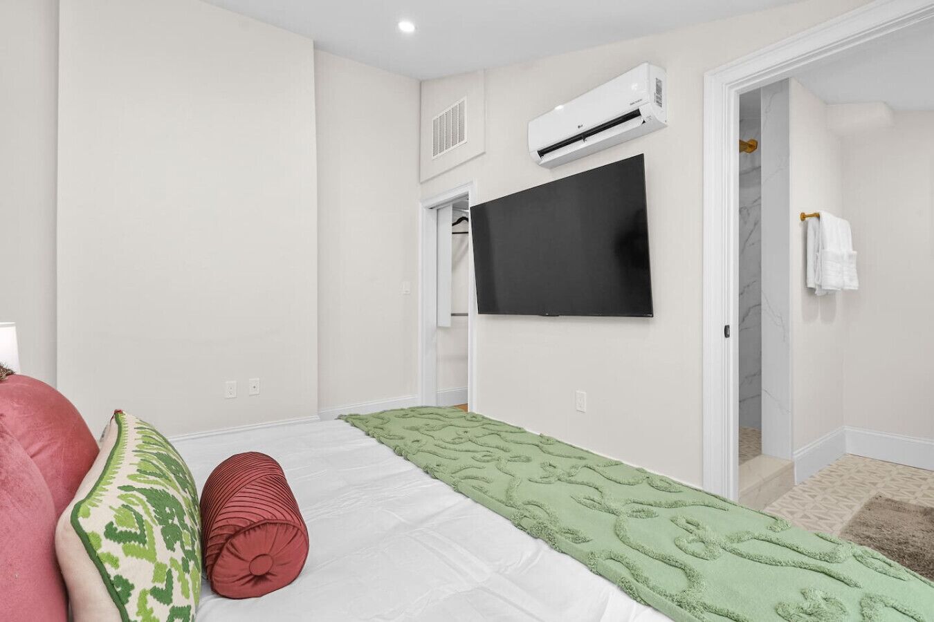 Ein Schlafzimmer mit Bett, Fernseher, Klimaanlage und einem durchgegangenen Tür sichtbaren Badezimmer.
