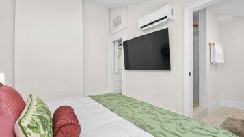 Ein Schlafzimmer mit Bett, Fernseher, Klimaanlage und einem durchgegangenen Tür sichtbaren Badezimmer.