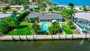 A residential area with a house featuring a swimming pool, surrounded by palm trees and a waterfront. - River House Retreat — Canal Views and Poolside Bliss! (Bradenton)