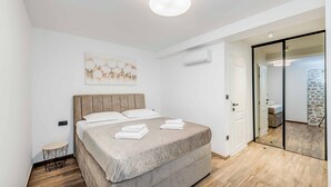 Een moderne slaapkamer met een groot bed, een klein nachtkastje, een plafondlamp en een schuifdeur naar een badkamer.