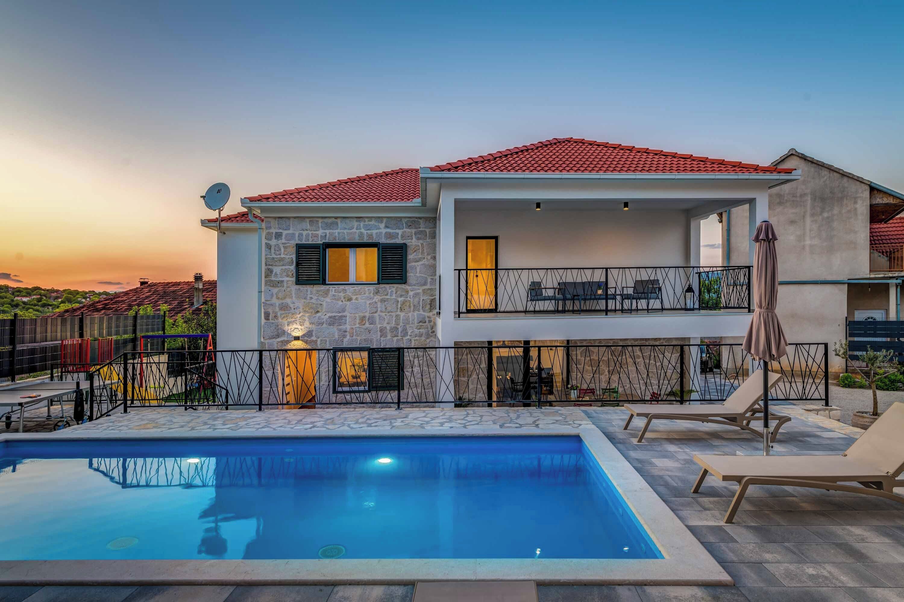 A two-story house with a swimming pool, outdoor seating, and a balcony.