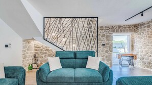 Een moderne woonkamer met een blauwgroene bank, stenen muren en uitzicht op een tuin.