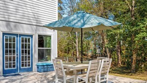 Une terrasse avec une table et des chaises, un parasol, et une maison aux portes et fenêtres bleues.