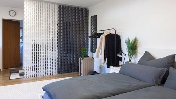 Un dormitorio moderno con una cama grande, un radiador, un perchero con ropa y una planta.