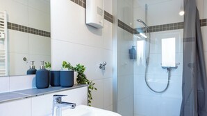 Un baño moderno con un lavamanos blanco, ducha con mampara de vidrio y un espejo sobre el lavamanos.