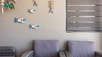 Una habitació amb mobles de vímet, una decoració de peix penjada a la paret i una finestra amb persianes horitzontals.