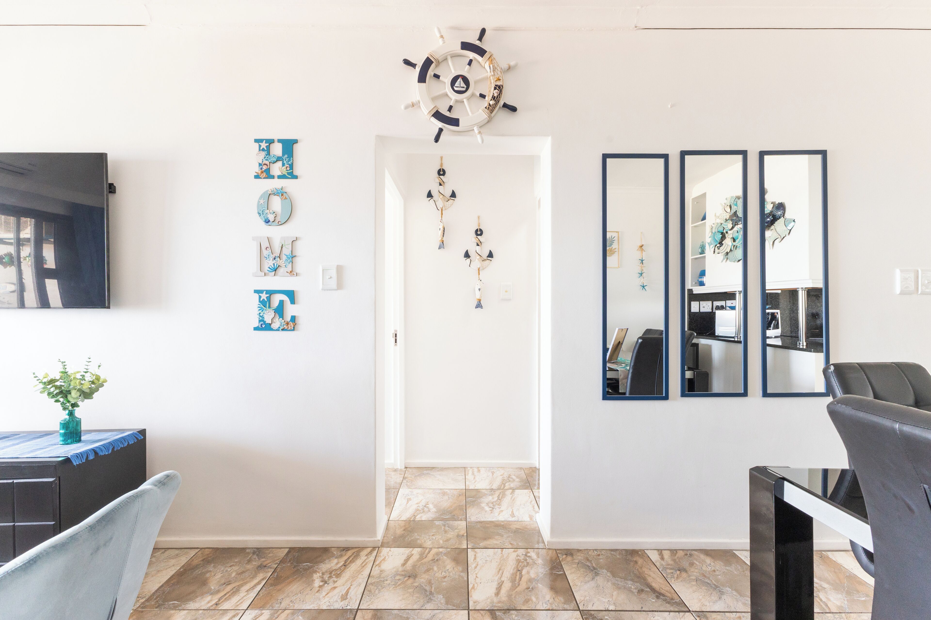 A modern living room with a TV, a dining area with a table and chairs, and a hallway leading to another room.