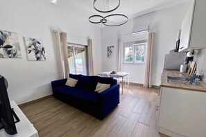 A modern living room with a blue sofa, a dining table, and a kitchen area.