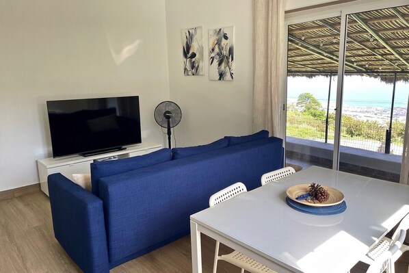 A living room with a TV, sofa, fan, table, and a scenic view through large windows.